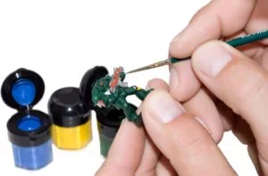 A set of hands holding a thin brush and a miniature while painting it