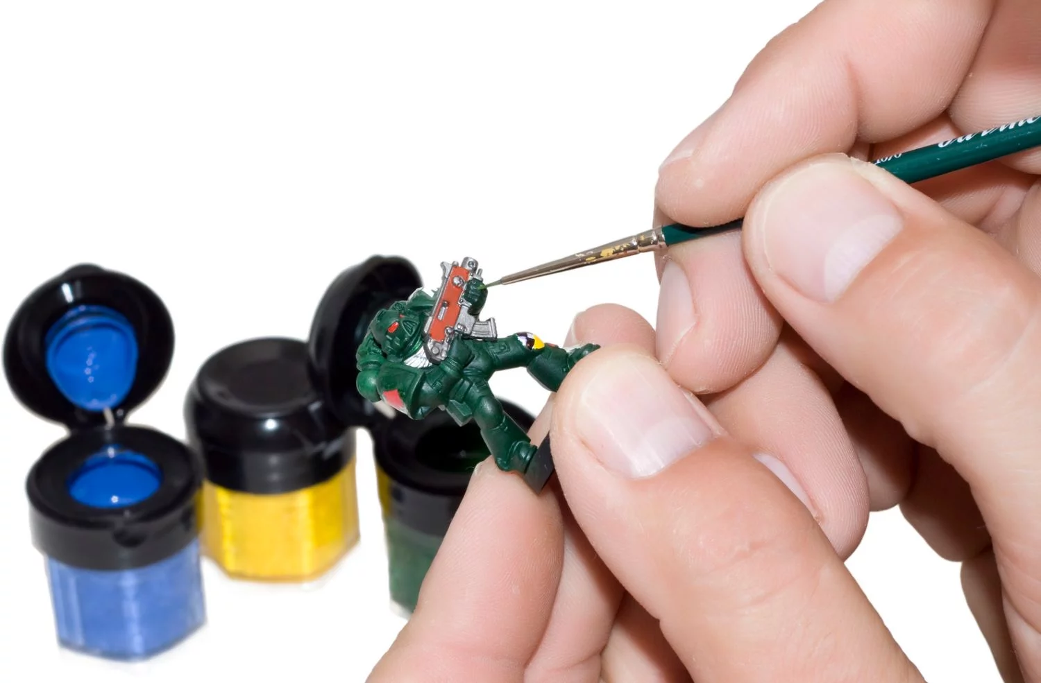 A set of hands holding a thin brush and a miniature while painting it