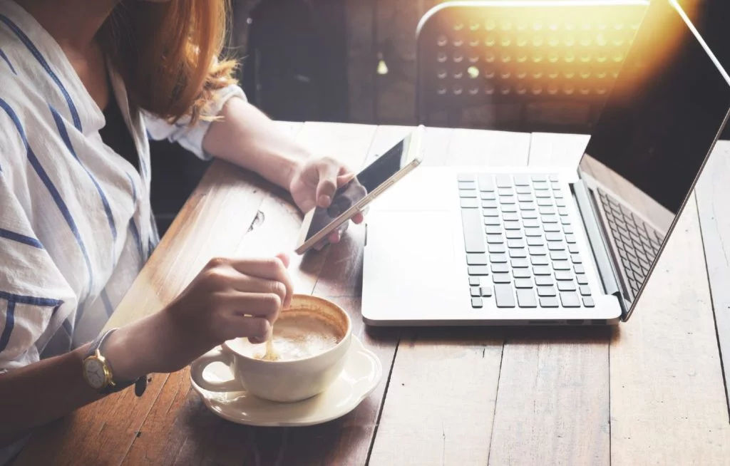 Woman working at a café with her smartphone in hand and a coffee